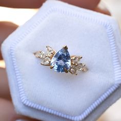 a blue and white diamond ring sitting on top of a white cloth covered box,