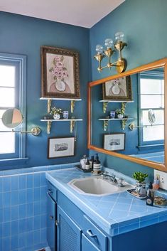 a bathroom with blue tile and gold fixtures on the wall, along with framed pictures