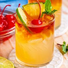 two glasses filled with drinks sitting on top of a table next to limes and cherries