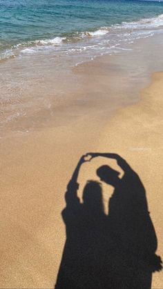 the shadow of a person standing on top of a sandy beach next to the ocean