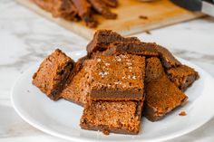 some brownies are on a white plate near a cutting board and utensils