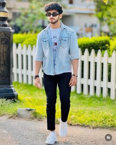 a young man walking down the street wearing black pants and a denim shirt with white sneakers