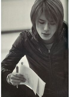 a young man holding a pen and paper in his hand while looking down at something