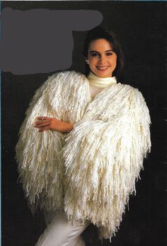 a woman wearing a white fuzzy coat with her arms crossed and smiling at the camera