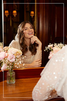 a woman sitting in front of a mirror next to a vase with flowers on it