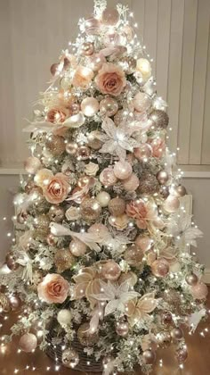 a white christmas tree with pink and gold ornaments on the top, surrounded by lights