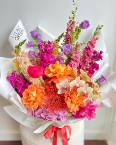 a bouquet of colorful flowers in a white vase with red ribbon on the bottom and side