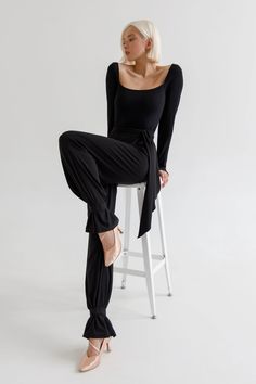 a woman sitting on top of a stool wearing black pants and a long sleeved shirt