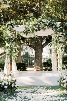 an outdoor wedding ceremony with white flowers and greenery on the ground under a tree