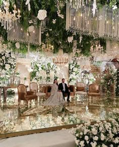 a bride and groom are sitting in the middle of a room with chandeliers hanging from the ceiling