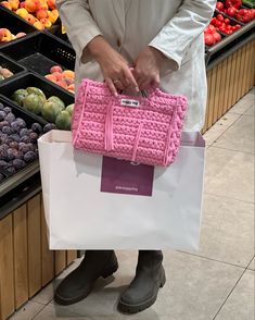 a person holding a pink purse in front of some fruit