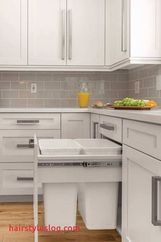 a kitchen with white cabinets and drawers has two trash cans in the middle of it