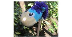 a knitted pony head hanging on a tree branch with leaves around it's base