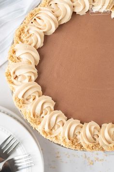 a chocolate pie with white frosting on a plate next to a knife and fork