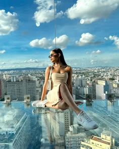 a woman sitting on top of a tall building in a tan dress and white sneakers