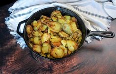 a skillet filled with potatoes on top of a wooden table next to a white towel