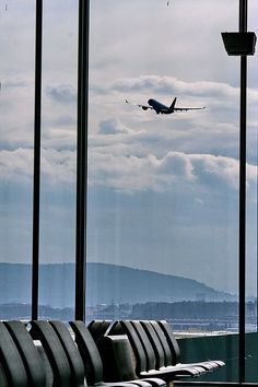 an airplane is flying in the sky over some seats at an airport with mountains in the background