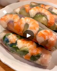 three shrimp spring rolls on a white plate with sauce and green peppers in the middle