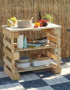 an outdoor table made out of wooden pallets with bowls and plates on it, next to a bamboo fence