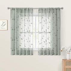 a window with sheer curtains in front of a white wall and wooden dresser next to it