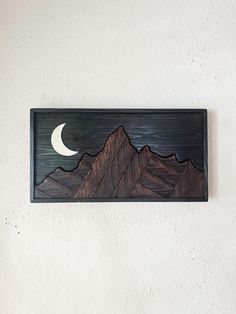 a wooden wall hanging with mountains and a half moon in the sky on it's side