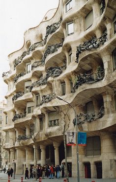 people are walking on the sidewalk in front of a building that looks like it is made out of concrete