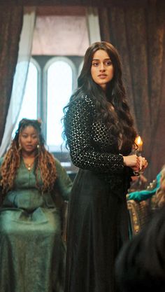 a woman in a black dress standing next to two other women and holding a lit candle