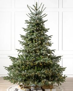 a christmas tree with lights and presents on the floor in front of a white wall