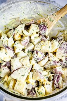 a glass bowl filled with potato salad on top of a white tablecloth and wooden spoon