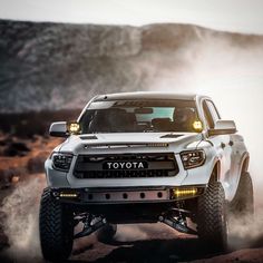 a white toyota truck driving down a road with fog coming off the ground behind it