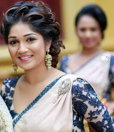 a woman in a blue and white sari smiles at the camera while another woman stands behind her