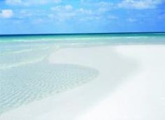 an empty beach with white sand and blue sky