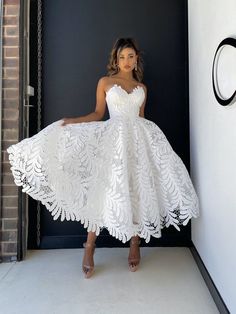 a woman standing in front of a black door wearing a white lace dress with one hand on her hip