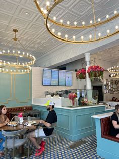 people sitting at tables in a restaurant with lights hanging from the ceiling and chandeliers