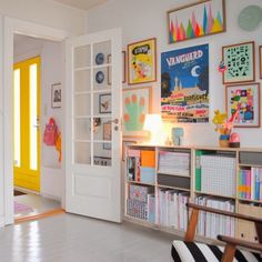 a room filled with lots of books and pictures on the wall next to a yellow door