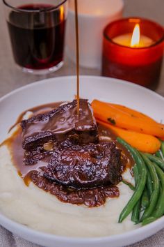 a plate with mashed potatoes, green beans and carrots next to a candle