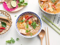 two bowls filled with soup next to chopsticks on a white tablecloth and bamboo utensils