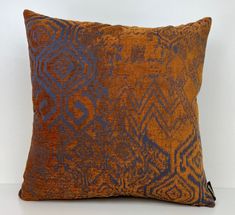 an orange and blue decorative pillow on a white surface with a black zippered closure