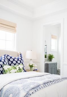 a white bed with blue and green pillows in a bedroom next to a mirror on the wall