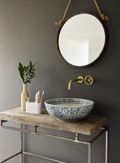 a bathroom sink sitting under a mirror next to a wooden table with a potted plant on it