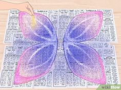 a butterfly made out of newspaper paper on top of a wooden table next to a person's hand