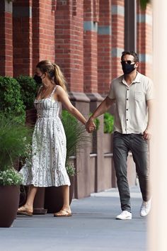 a man and woman holding hands while walking down the street with masks on their faces