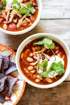 three bowls of chili and bean soup with cilantro garnish on the side