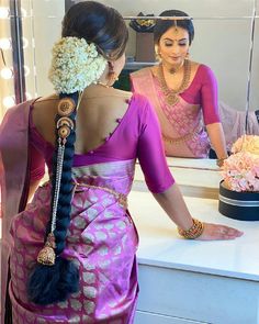 a woman in a pink sari is looking at her reflection in the mirror while another woman looks on