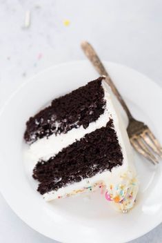 a slice of chocolate cake with white frosting and sprinkles on a plate