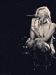 a black and white photo of a woman sitting on a stage with her legs crossed