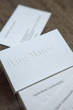 two white business cards sitting on top of a wooden table with the word bag marco printed on them