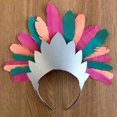 a paper crown with feathers on it sitting on top of a wooden table next to scissors