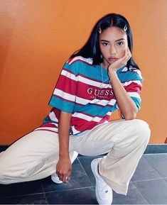 a young woman sitting on the ground in front of an orange wall with her hand under her chin