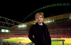 a man standing in front of a baseball field at night with his hands on his hips